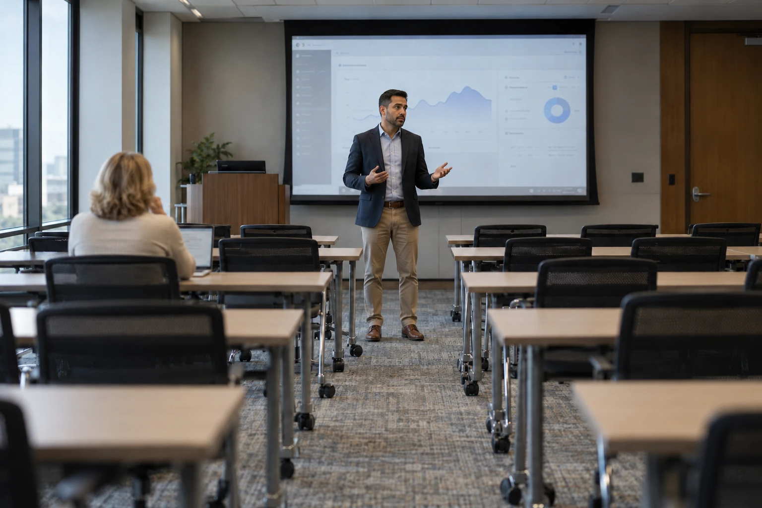 A trainer presenting to a nearly empty training room, one attendee at a laptop